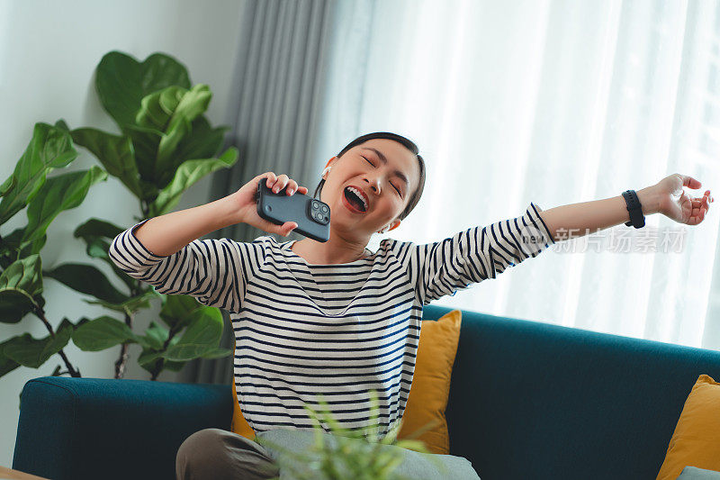 快乐的女人在家里用智能手机和耳机听音乐。