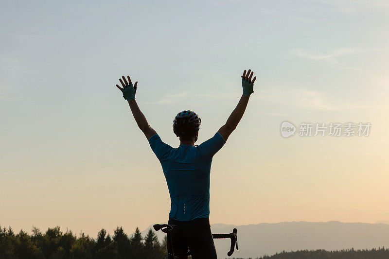 自行车手高举双臂庆祝胜利，后景