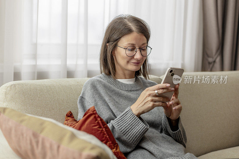 年轻的成年女子坐在客厅的沙发上玩手机