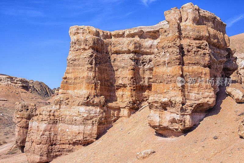 哈萨克斯坦沙漠中巨大的查林峡谷。画面中央是一座巨大的孤立的山和岩石，映衬着蓝天和细细的云朵