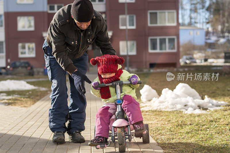 70岁的老人，活跃的爷爷，教他的孙女，2岁的小女孩，如何骑自行车在寒冷和阳光明媚的冬日散步。
