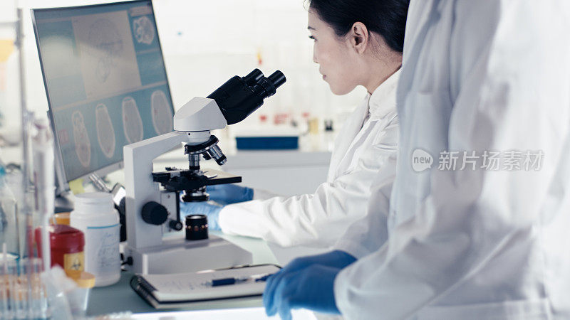 未来实验室内部。亚洲女医生在基因研究期间与伴侣