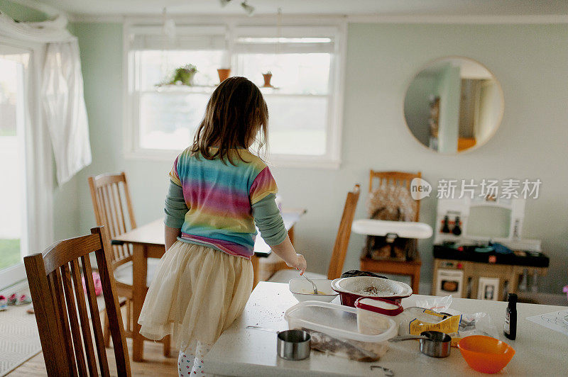 穿着彩虹衬衫和褶边裙的小女孩在厨房柜台烘焙