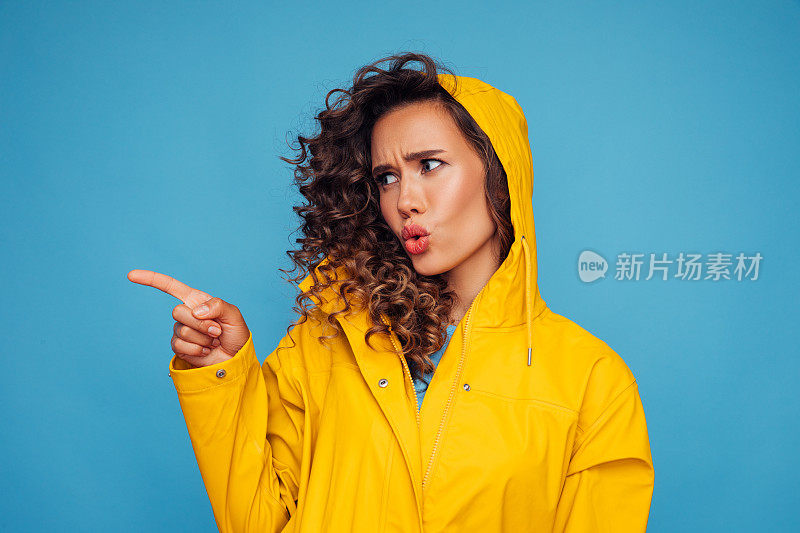 美丽失望的女人穿着黄色雨衣指向远方