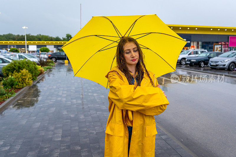 年轻女子拿着黄伞站在雨中