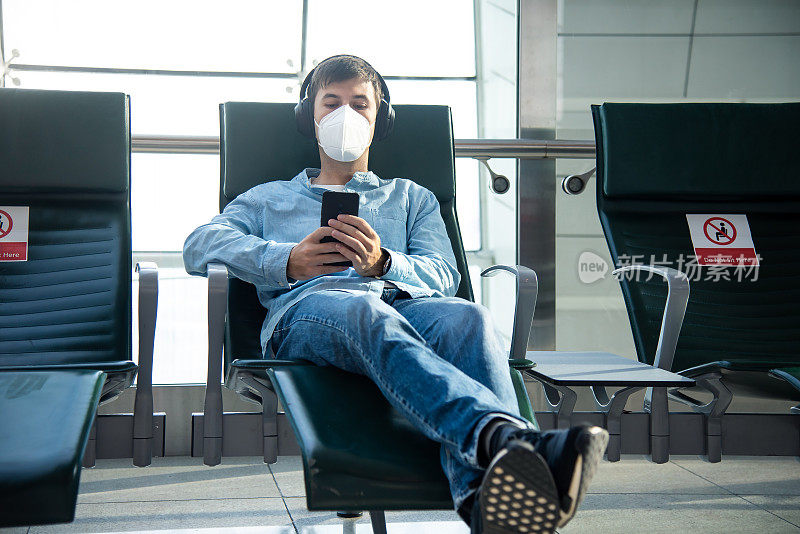 一名戴着口罩在机场大厅等候时打电话的男子