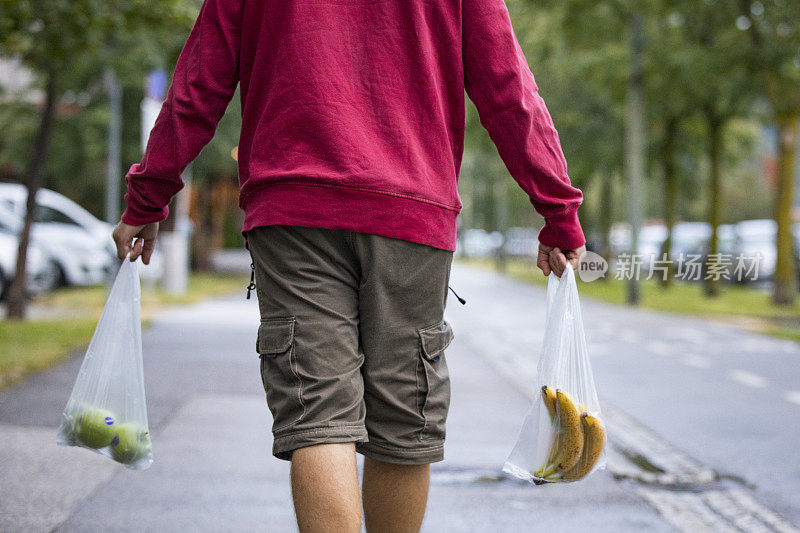 一个年轻人在城市街道上用购物袋提着水果