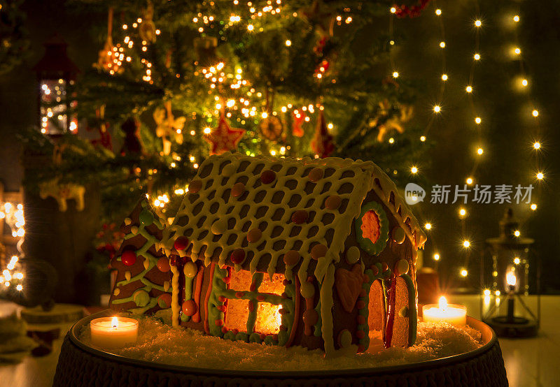 有趣的彩色装饰和色彩丰富的姜饼屋焦糖玻璃窗和蜡烛照亮内部，模糊的散景圣诞树和客厅的背景。