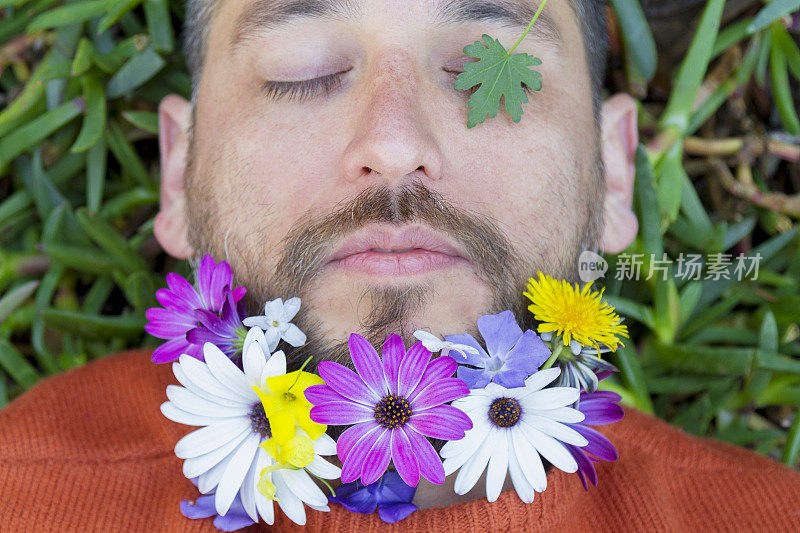 英俊英俊的拉丁男性肖像与春天的鲜花在他的胡子放松躺在绿色的草