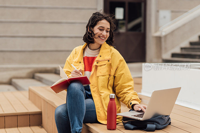 一个女孩坐在她的大学门口，在网上学习