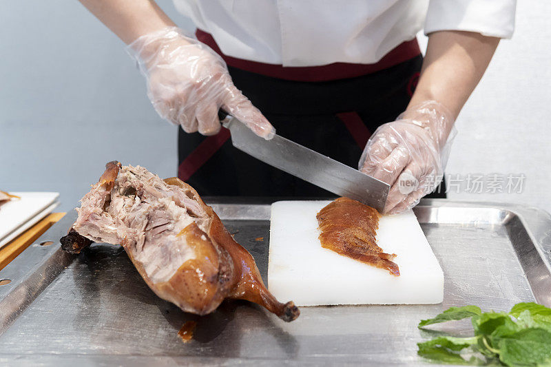 一位厨师在一家餐馆的厨房里切着美味的北京烤鸭