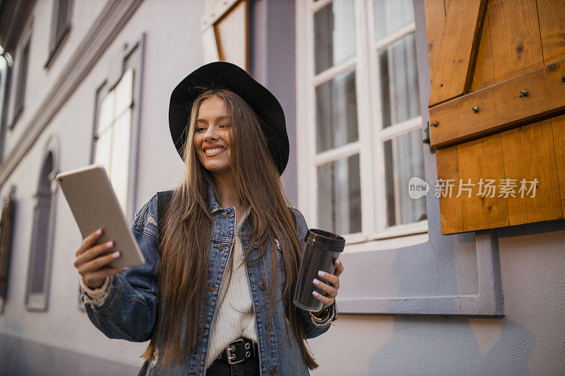 年轻女子喝着咖啡，在街上用着平板电脑