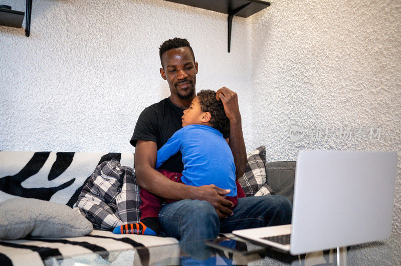 一位单身父亲在家工作时安慰坐在他腿上的儿子