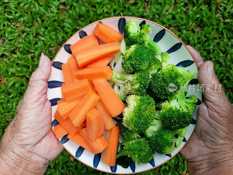 老人手拿一盘西兰花和胡萝卜。