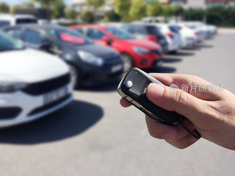 一名男性手持汽车钥匙，背景为离焦的停车场