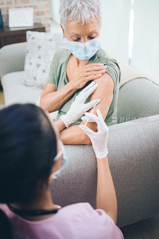 一名医生在家里给一名戴面具的老年妇女打针