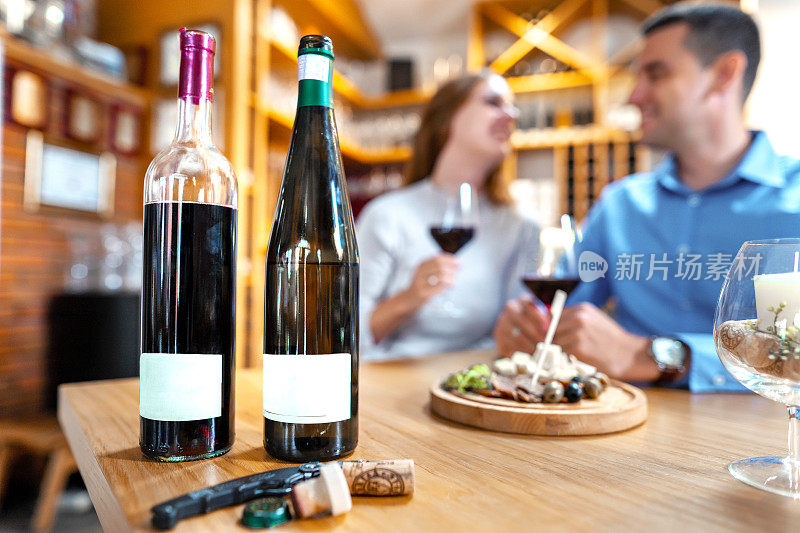 近距离照片的两个酒瓶与模糊的背景浪漫的夫妇品尝葡萄酒