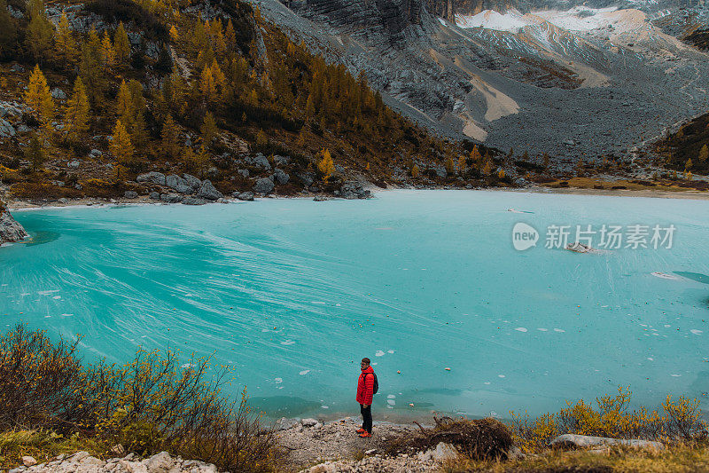 男旅行者呆在岩石上，凝视着阿尔卑斯山上冰封的高山湖泊的风景