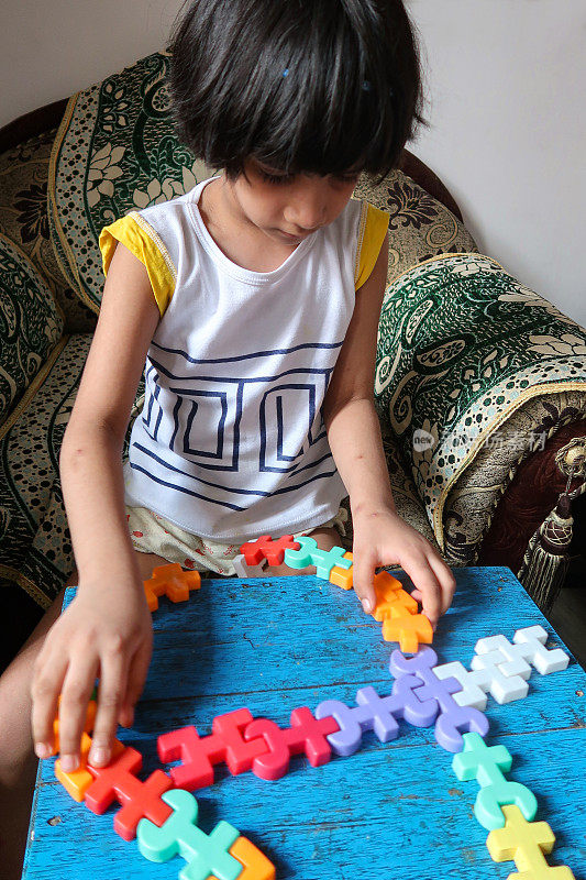 印度女孩坐在扶手椅上玩桌上的拼图玩具，低头看着游戏，注意力集中