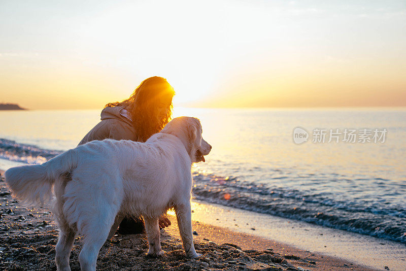 一个年轻女人和一只金毛猎犬在海滩上