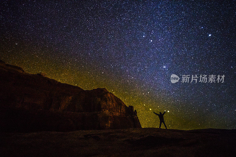 这个小个子男人站在无尽的宇宙前面。犹他州拱门国家公园山上的人的剪影，映衬着星空