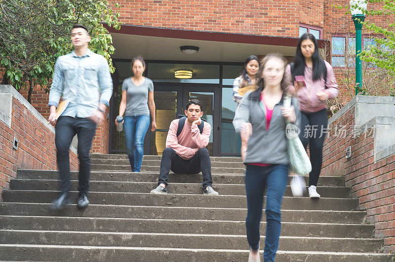 一名年轻的少数民族大学生在得知最后一次考试成绩后坐在台阶上，而学生们从他身边走过