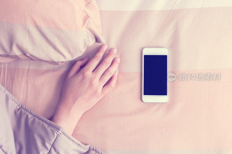 女人把手放在毯子下面被手机吵醒。