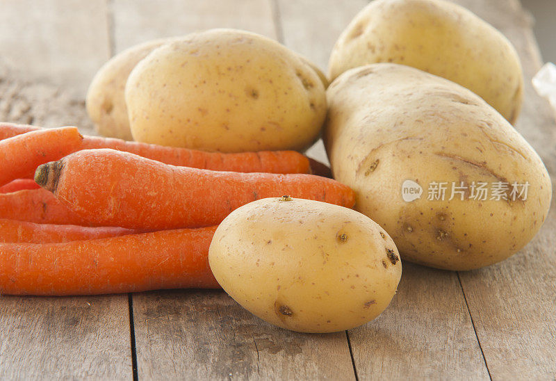 木片背景上放年轻的土豆和胡萝卜