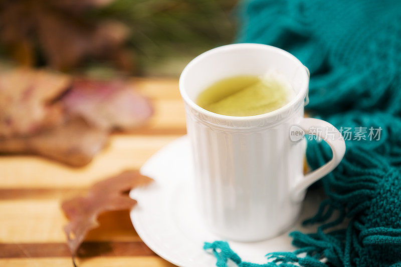 凉茶，白色杯子。秋天的落叶，绿围巾。木制的桌子。