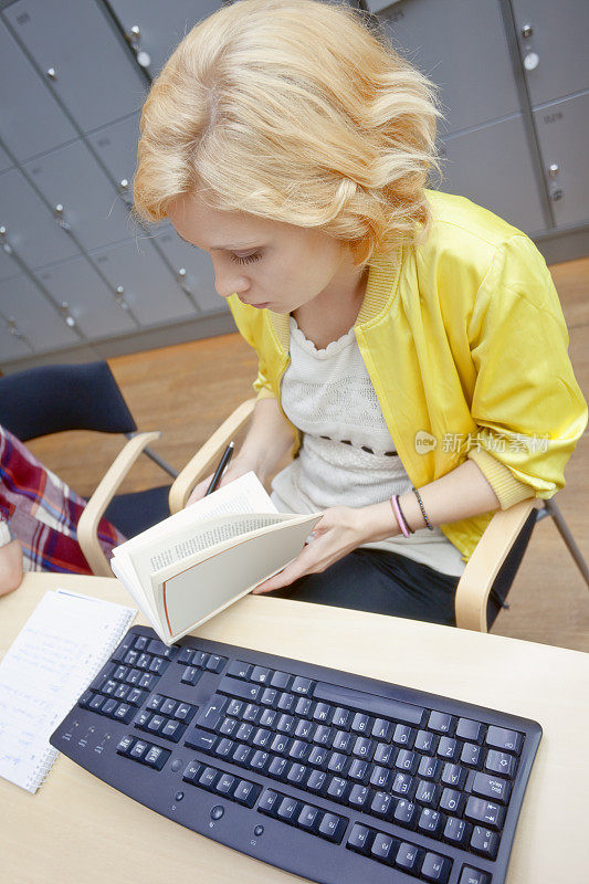 女学生在图书馆看书，计算机键盘在前台