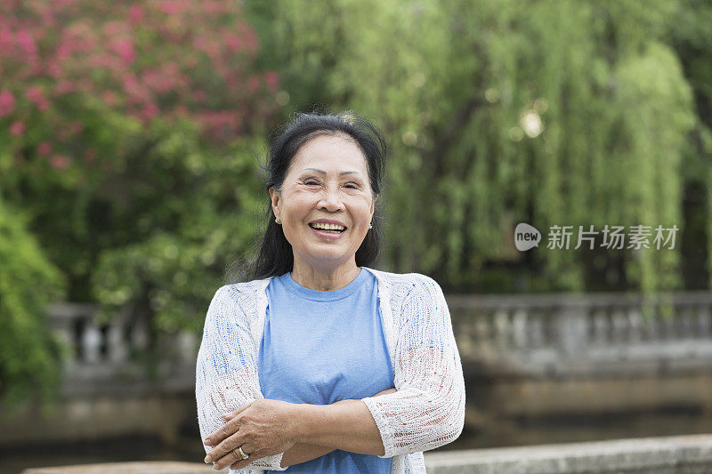 一位年长的亚洲女性双臂交叉站在公园里