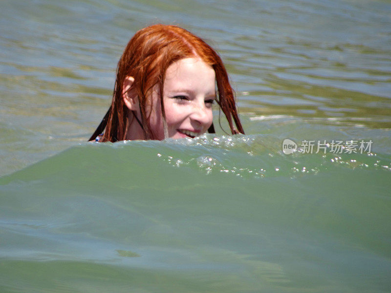 一个女孩在海里游泳，笑着，被海浪溅起