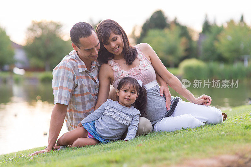 怀孕的夏威夷夫妇与年幼的女儿在公园户外依偎