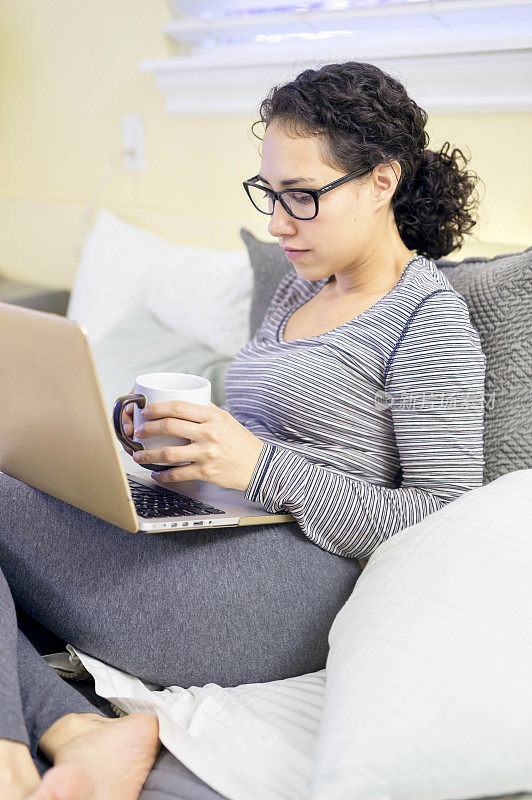 年轻的成年女性喝茶和使用笔记本电脑