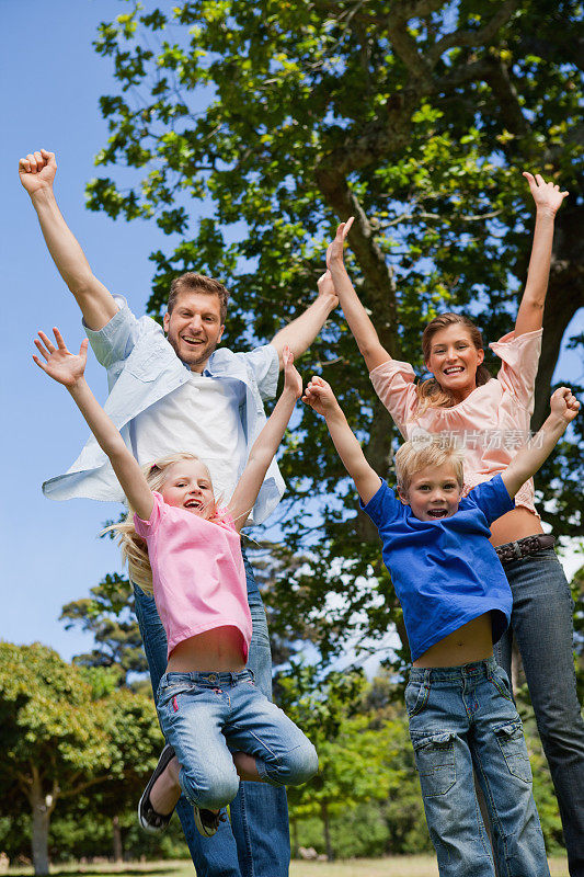快乐的一家人在公园里举起手臂跳跃