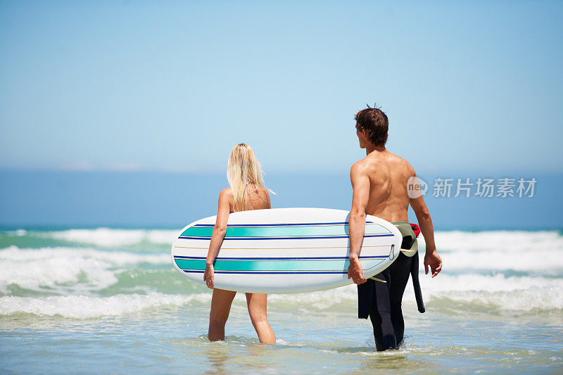一个男人和一个女人带着冲浪板在海浪中行走