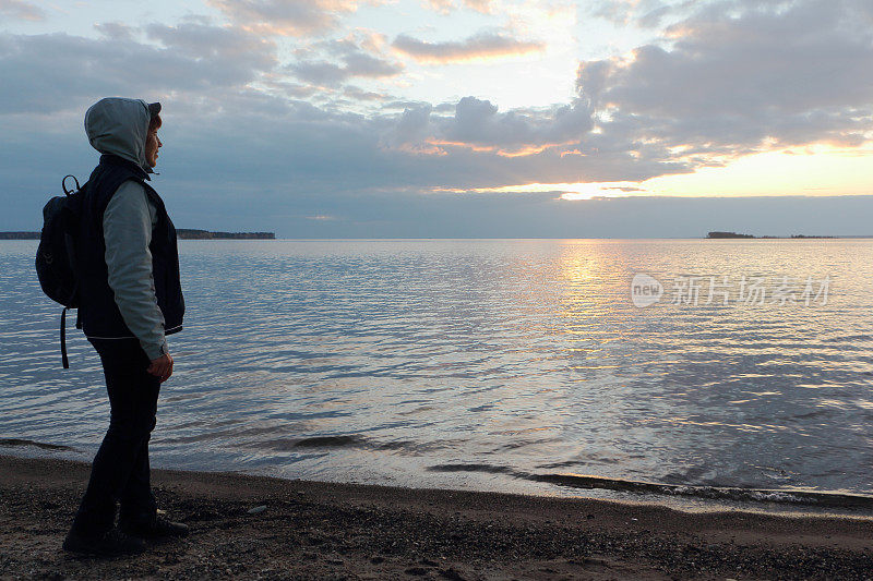 一个背着背包的女人站在日落时分的河岸上，鄂毕河，西伯利亚，俄罗斯