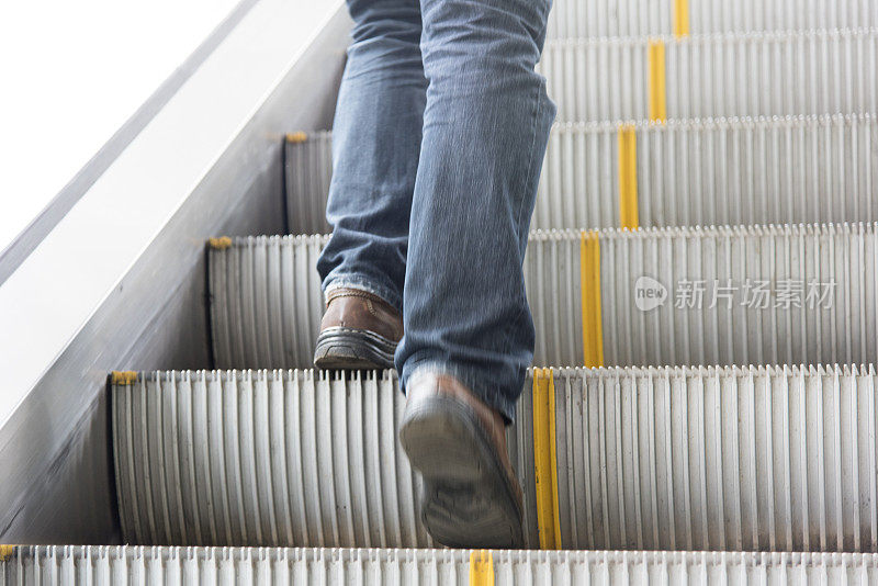 男士穿牛仔裤、皮鞋。站在自动扶梯上