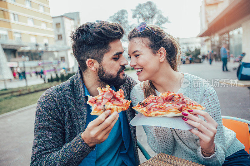 快乐的年轻夫妇在户外吃披萨。