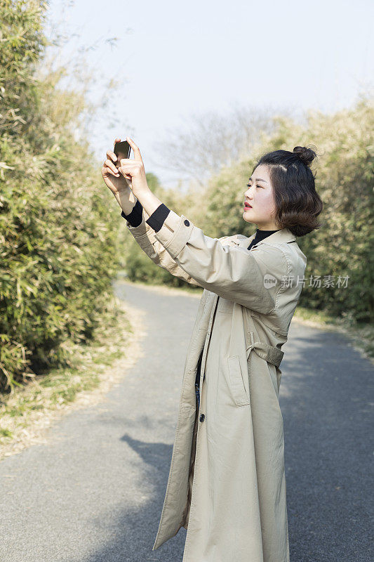 一名女子在公园小径上用智能手机拍照