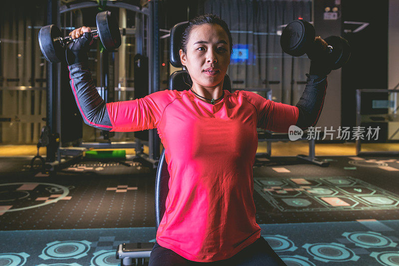 亚洲妇女在健身俱乐部用哑铃锻炼