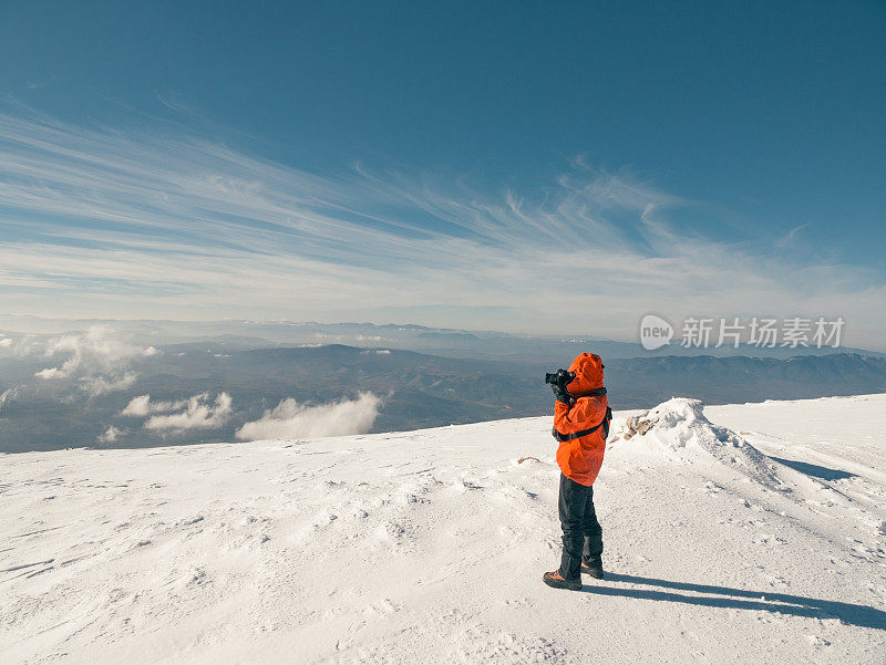 冬季日出时，女性高山攀登者在高海拔的山峰上拍照