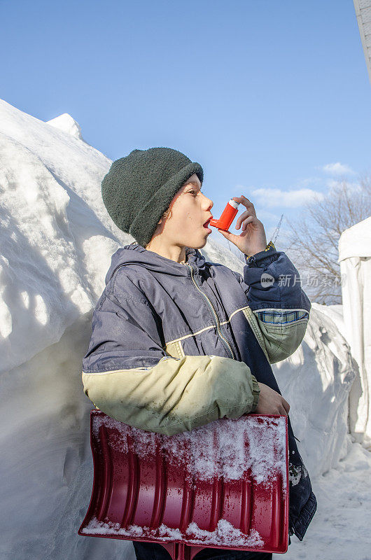 小男孩在铲雪后使用哮喘泵