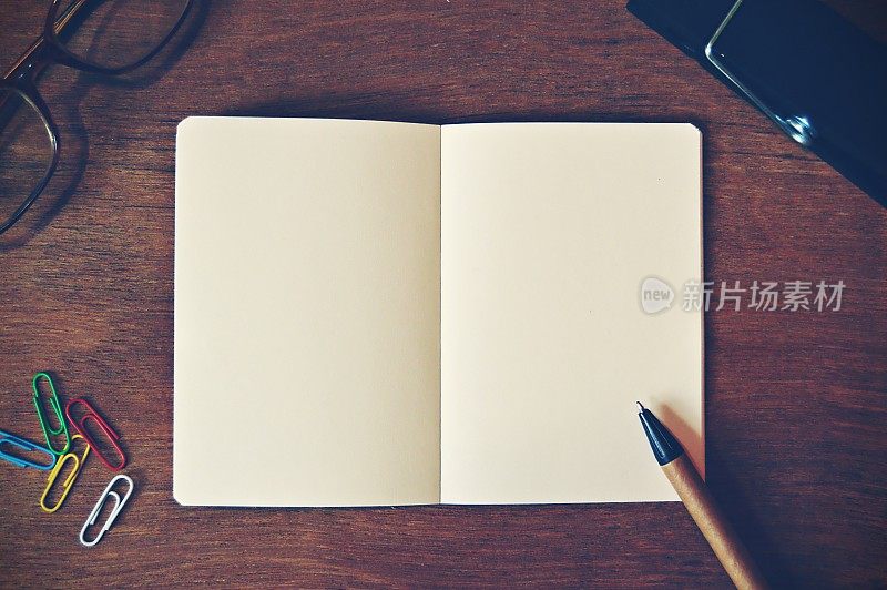 一张水平的照片，一张白色的素色记事本，一张棕色和黑色的钢笔和彩色回形针，眼镜放在一个木制的米色水平背景上，很有美感。