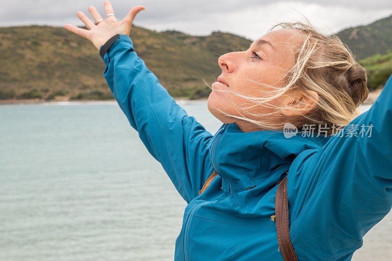 拥抱着雨，在暴风雨的天空下的海滩上，一个女人抬起双臂拥抱大自然