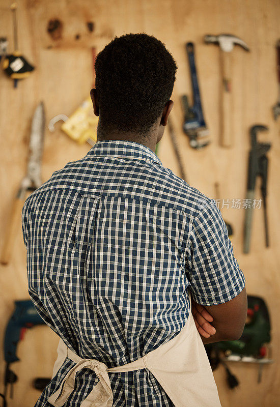 非洲裔美国木匠选择工具。设计师站在工具和设备的墙上。创造性的企业家决定使用工具。商人选择设备。