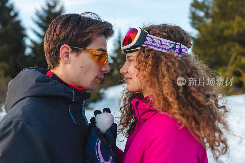 一对美丽的年轻夫妇在雪山的山顶上接吻的特写在他们的滑雪假期