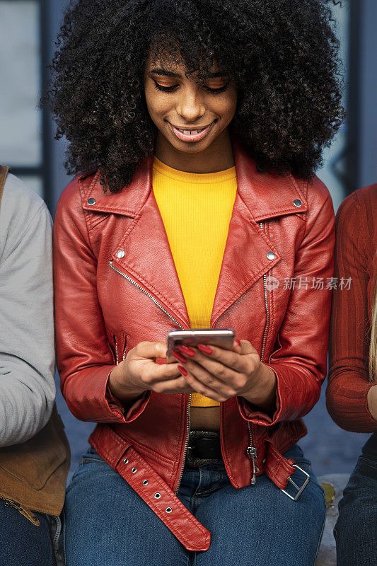 年轻的非洲裔美国女性坐在户外，使用智能手机——年轻人沉迷于互联网和新技术的生活方式概念