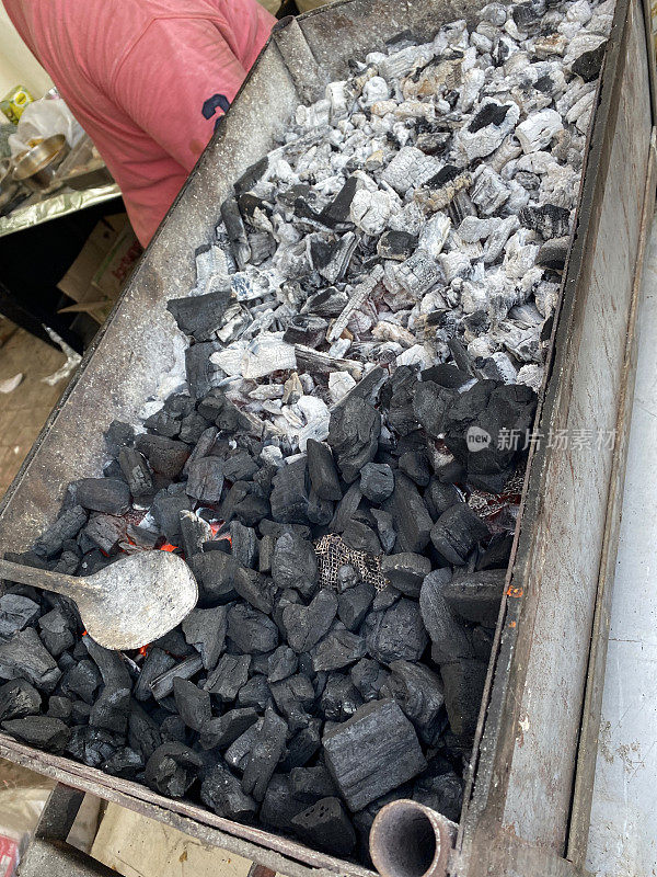 特写图像的金属烧烤托盘充满了热木炭的余烬和灰烬，火焰带来焦炭加热做饭，升高的观点，重点在前景