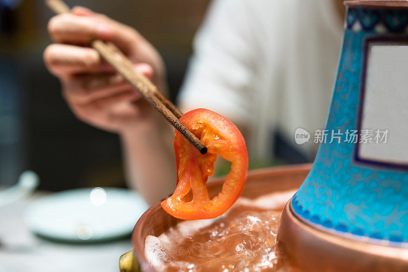 一只手拿着筷子，把西红柿放进火锅里